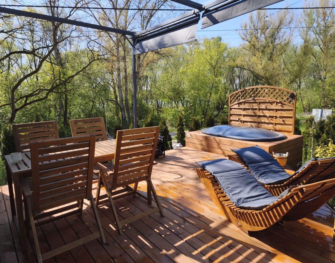 Drewniany taras z jacuzzi, leżakami i widokiem na zieleń nad Wisłą